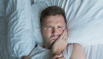 Man lying in bed with dental pain; dental emergency in Tulsa, OK