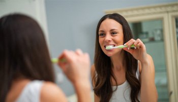 Woman looking in mirror and brushing her teeth