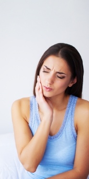 Woman in blue tank top holding her cheek in pain