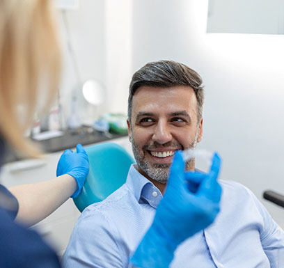 Tulsa dentist holding Invisalign aligner with smiling patient