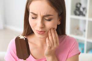 Woman with ice cream bar rubbing jaw due to sensitivity
